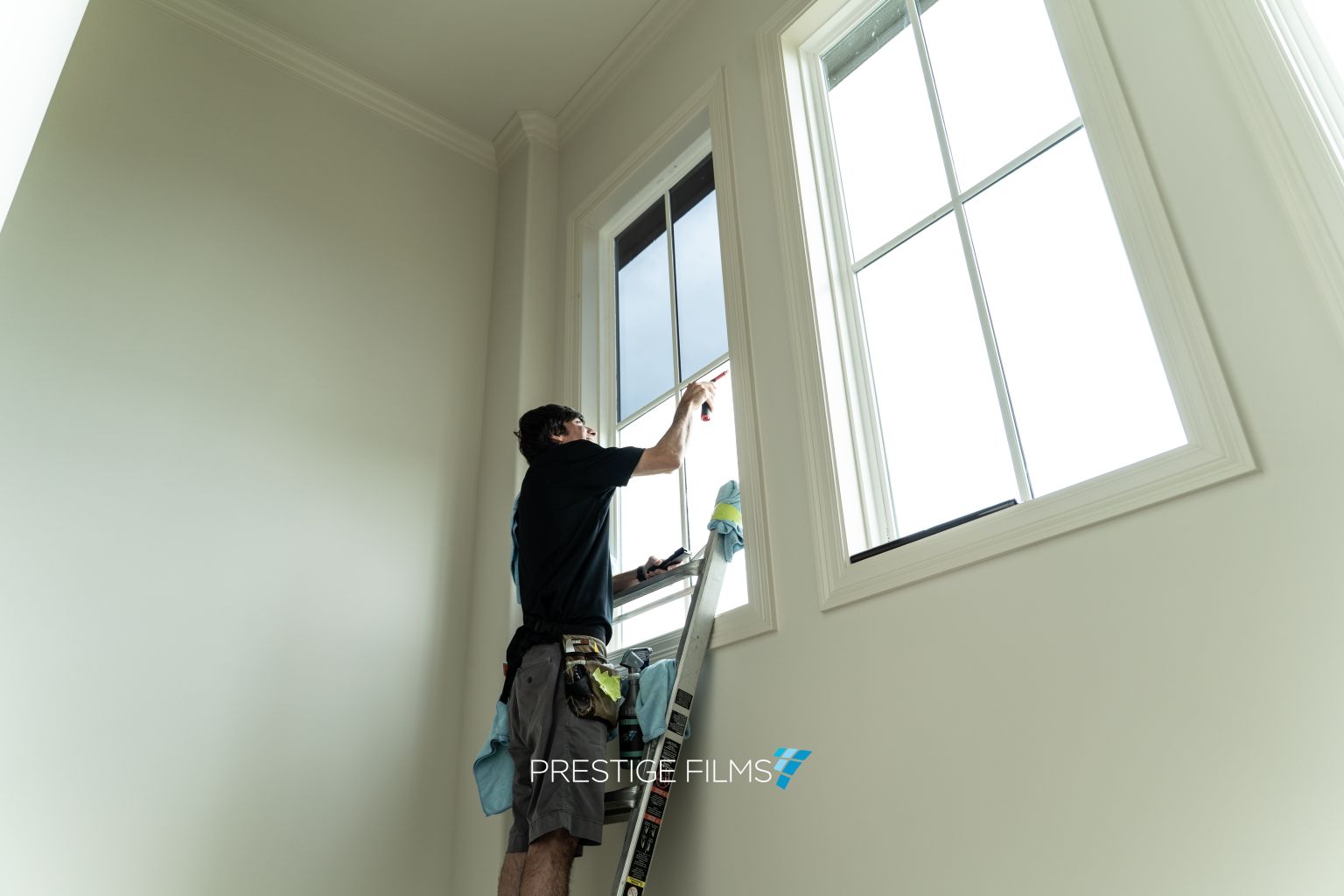 Installer on a ladder applying window film to a tall home window