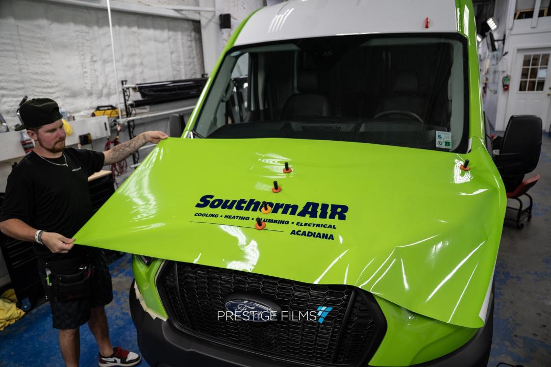 Installer applying a printed Southern Air wrap to a lime green work van
