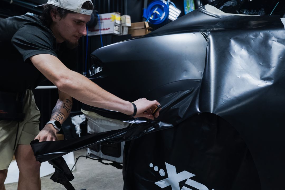 Prestige Films installer stretching matte black film over a car's rear quarter panel in the Lafayette shop
