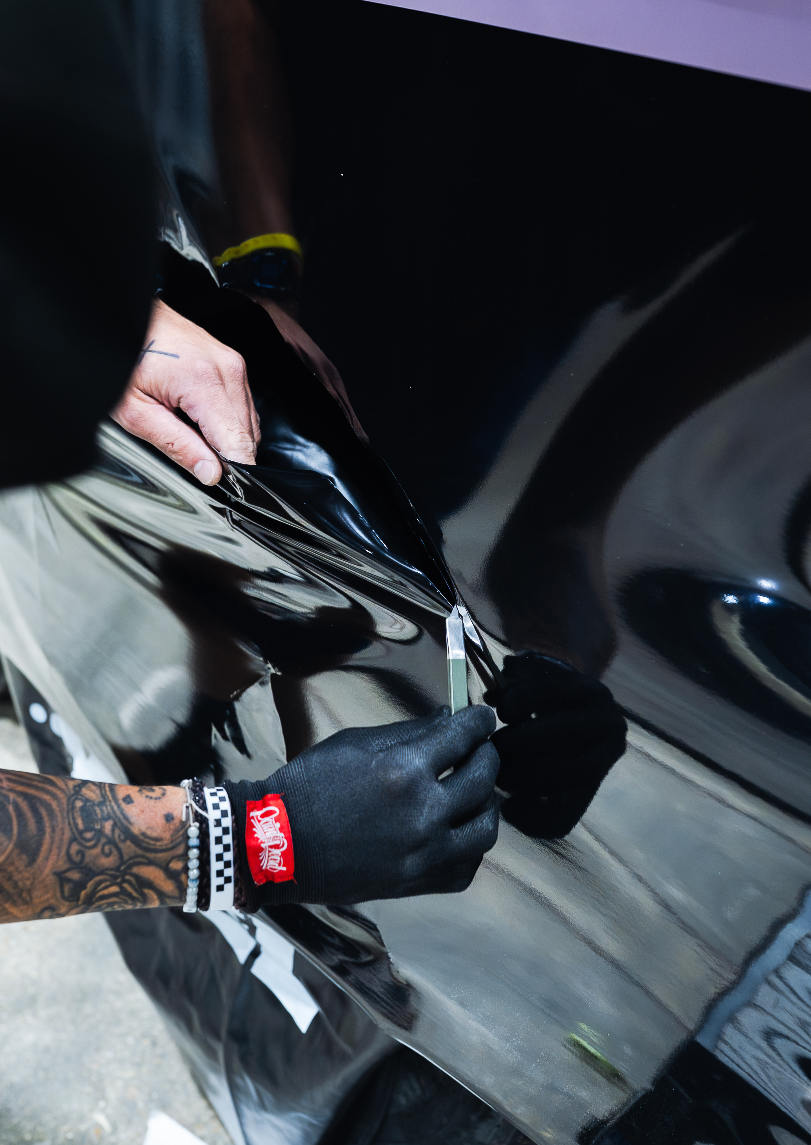 Gloved hands trimming black film around a car's door handle