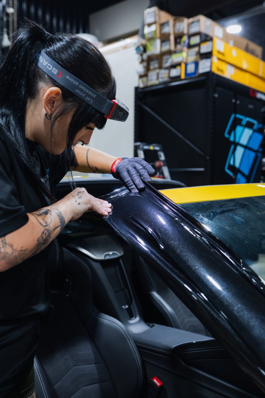 Installer applying single color black vinyl wrap to a yellow car