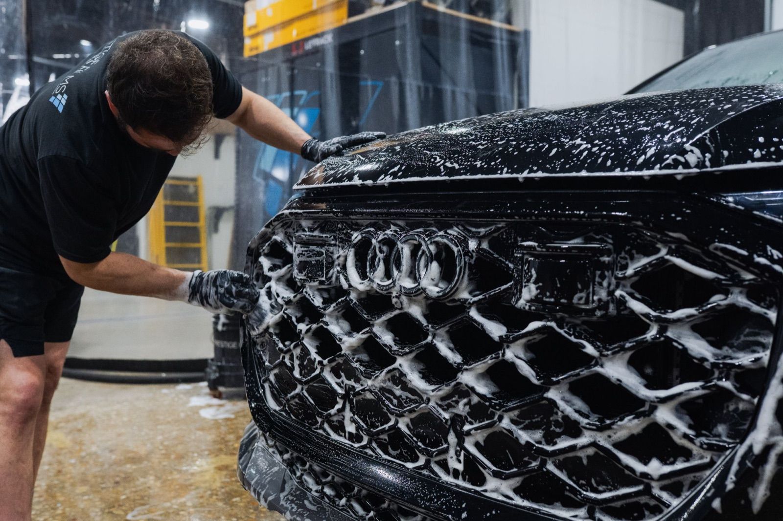 Technician foam-washing the front grille of a black Audi during decontamination prep
