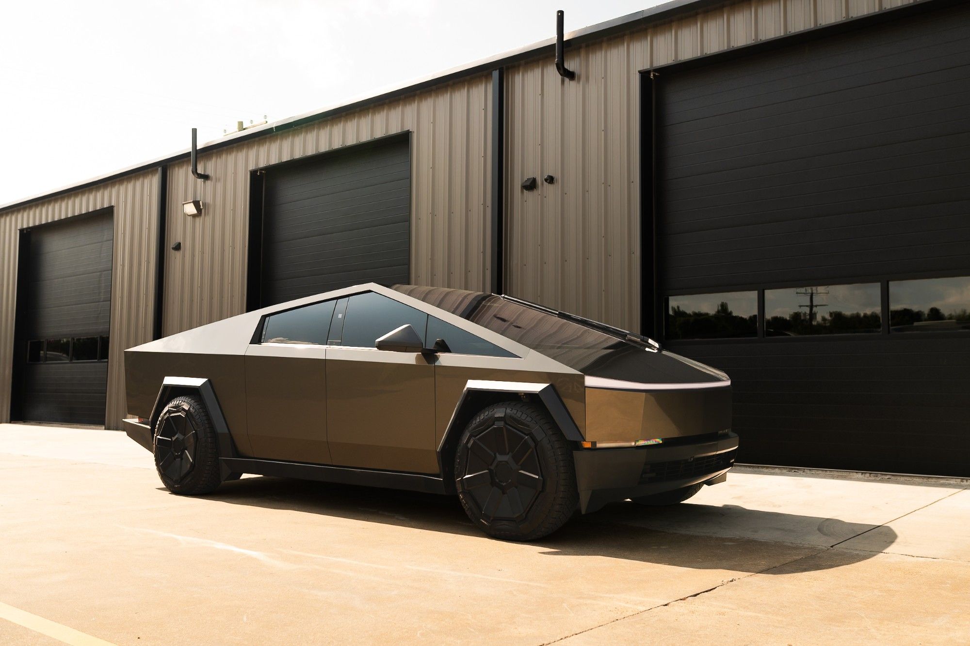 Contact hero – Tesla Cybertruck - Prestige Films Dark bronze Tesla Cybertruck parked outside a metal building with black garage doors