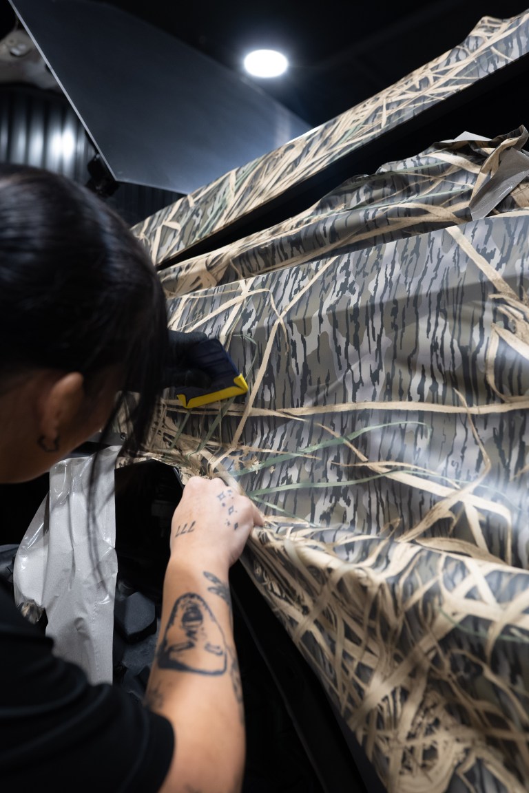 Installer applying a camo vinyl wrap to the side of a Tesla Cybertruck
