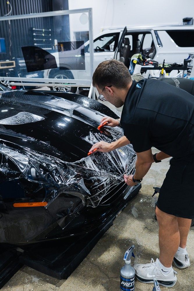 Installer stretching paint protection film over the front of a black sports car
