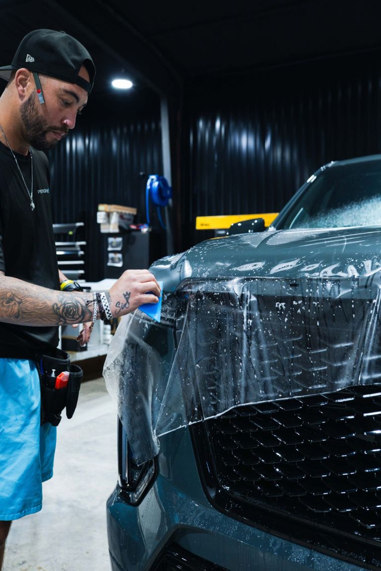 Installer squeegeeing paint protection film over the headlight of a gray Cadillac SUV