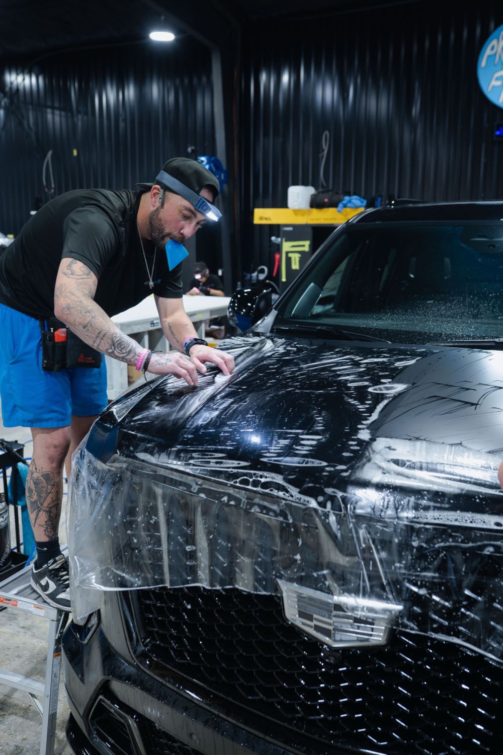 Prestige Films installers applying XPEL paint protection film to the front end of a black car