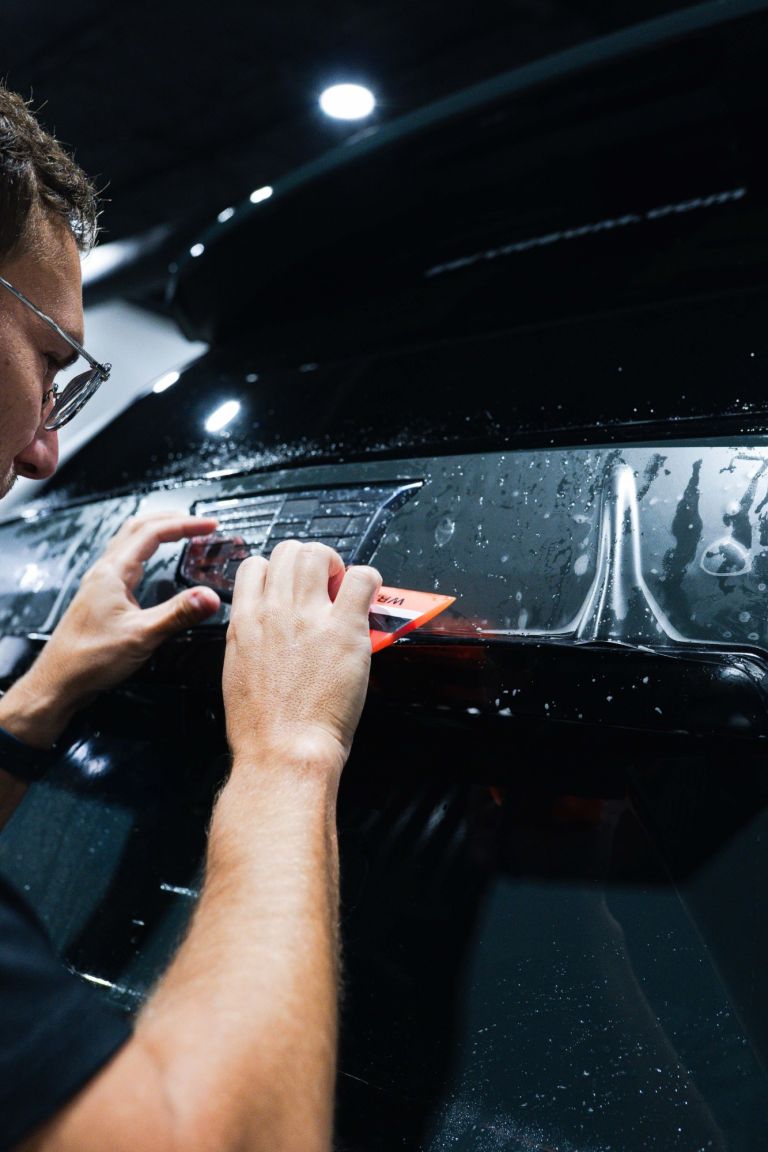 Installer working paint protection film around a rear badge with an orange squeegee