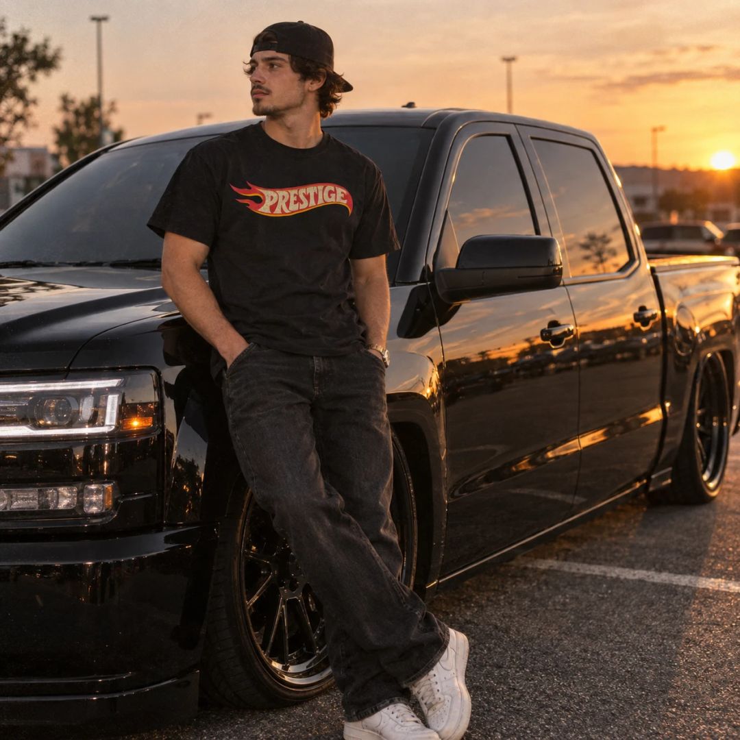 Man in the Prestige Flame Tee leaning on a lowered black pickup truck at sunset