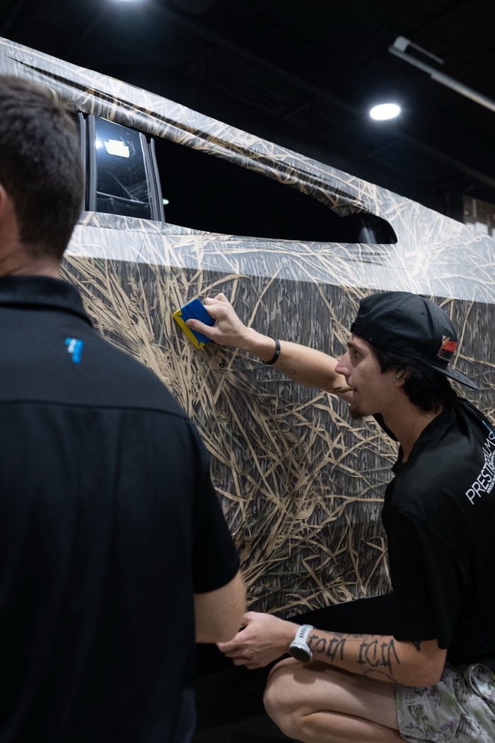 Installers applying a printed camo vinyl wrap to a Tesla Cybertruck