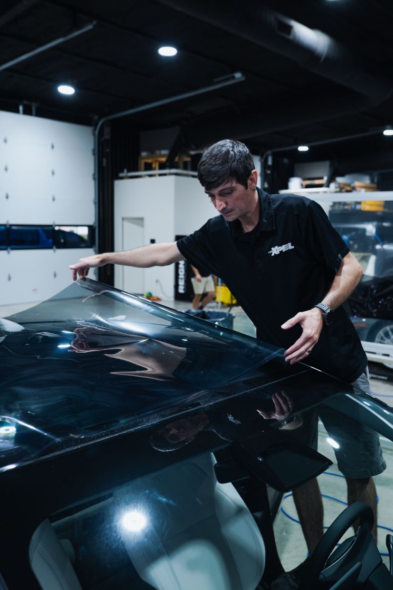Installer laying a large sheet of window tint film across a car's back glass