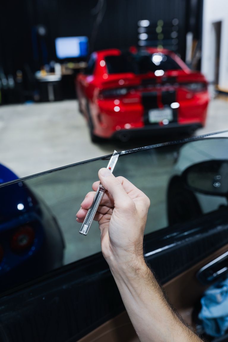 Close-up of an installer trimming window tint film along a car's door glass with a precision knife