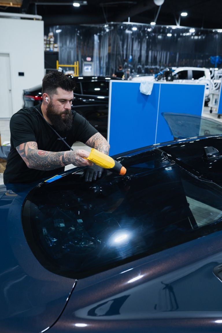 Installer heat-shrinking window tint film to the curved back glass of a dark blue car
