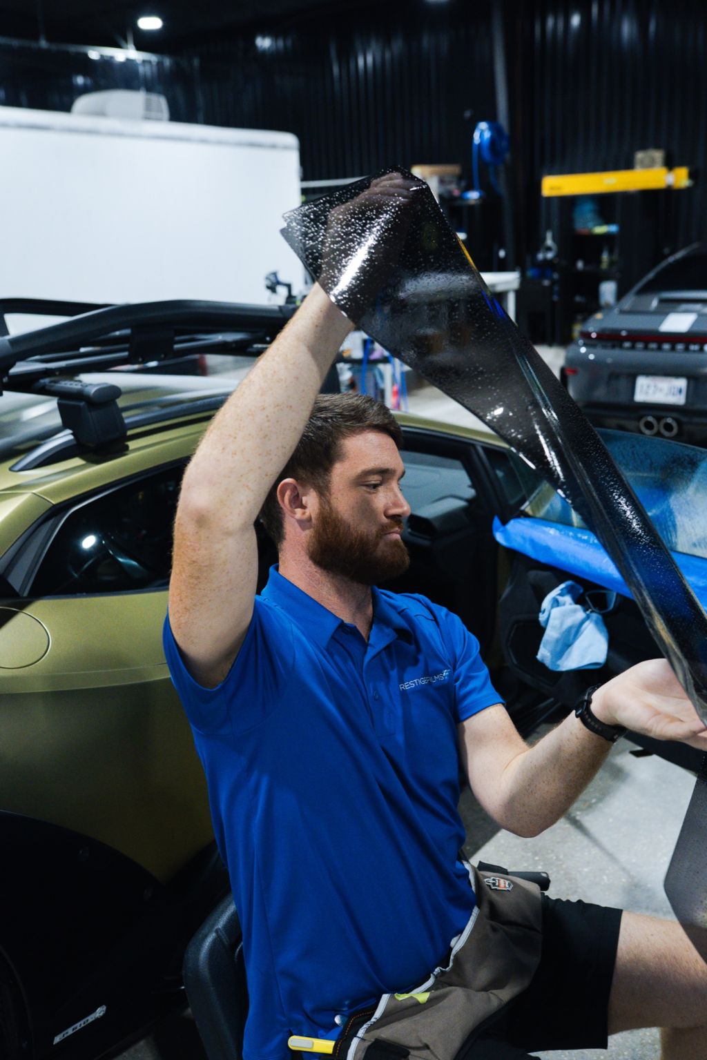 Installer lifting a sheet of window tint film into the door of a gold Lamborghini Huracán Sterrato